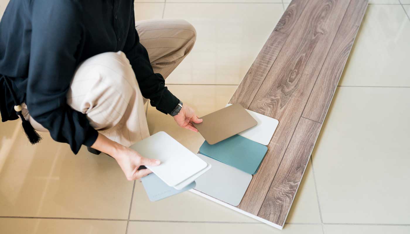 Someone comparing color swatches to a piece of flooring