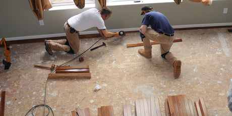 Two men preparing a wood sub-floor before flooring installation.